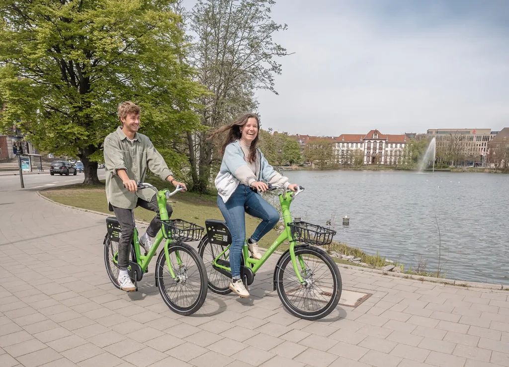 Zwei Personen, die auf den grünen Rädern der SprottenFlotte vor dem Kleinen Kiel zu sehen sind